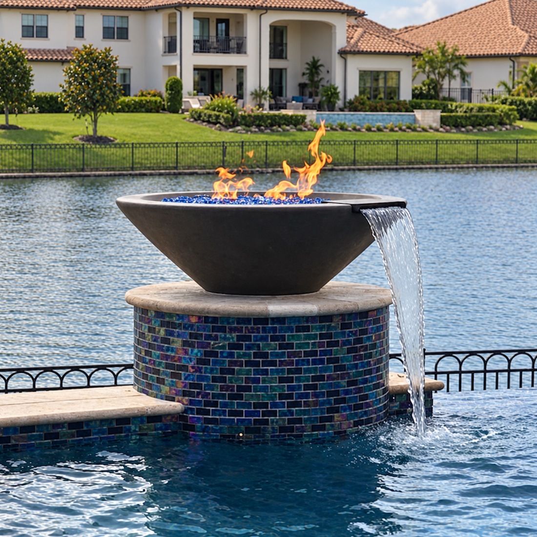 Cazo GFRC concrete fire and water bowl on a mosaic tile pillar, spilling water into a waterfront pool