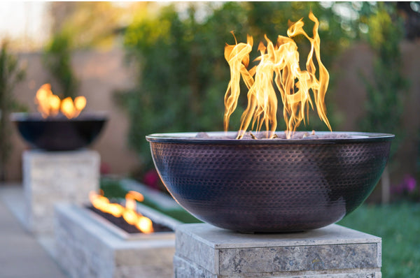 Hammered copper gas fire bowls on stone pedestals in a garden