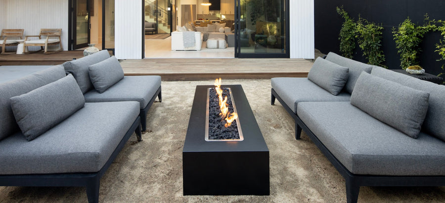 The Outdoor Plus black linear gas fire pit between two grey outdoor sofas on a modern patio