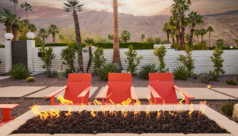 Long linear gas fire pit in a desert backyard with palm trees and orange lounge chairs